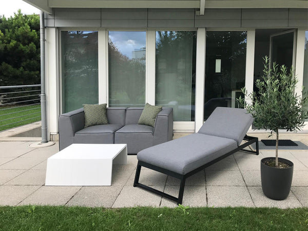 Outdoor patio with gray sectional sofa, lounge chair, and white coffee table on a patio.