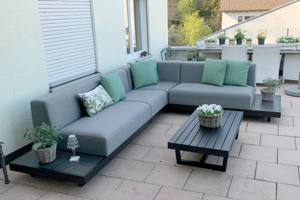 Outdoor patio with gray sectional sofa, green cushions, and a wooden coffee table.